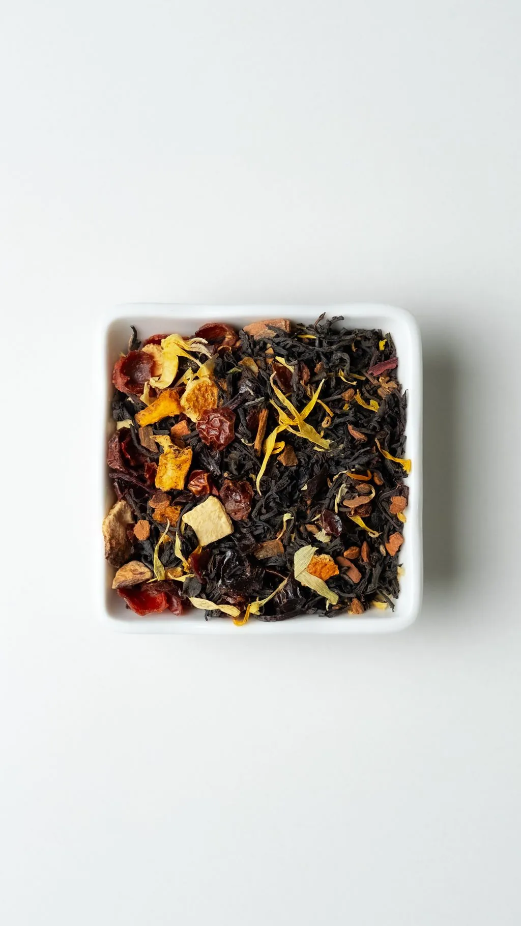 Pumpkin Spice loose-leaf tea with dried fruit and spices in a white dish on a clean near-white background.